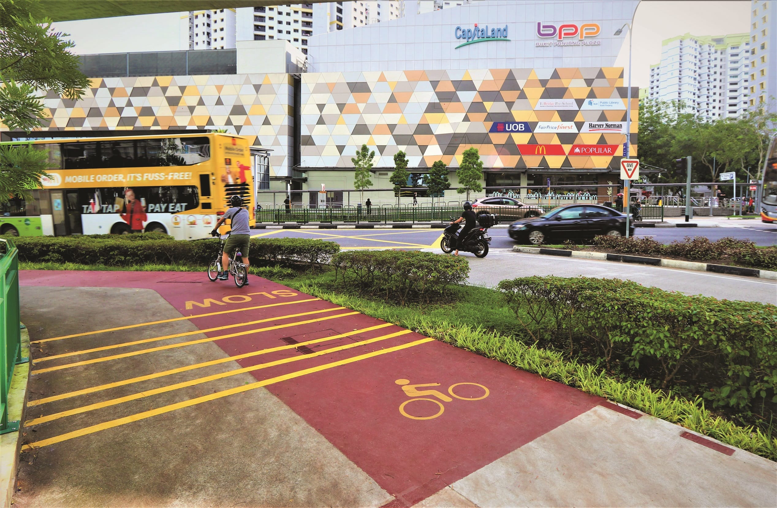A cyclist on a marked bike path near Bukit Panjang Plaza, with a bus and other traffic in the background.